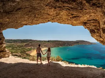 Para w jaskini podziwia widok na turkusowe morze i plażę. Malta pogoda wrzesień idealna na wakacje.