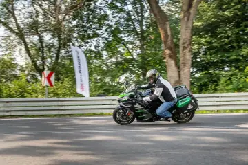 Motocyklista na czarnym Kawasaki Ninja H2 z zielonymi akcentami mknie po drodze, otoczony drzewami.