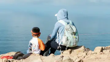 Chłopiec w pomarańczowej opasce i mama z plecakiem patrzą na morze. To idealny ekwipunek dla dziecka na wycieczkę.