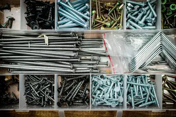 Pudełko z narzędziami pełne gwoździ do drewna, śrub i metalowych kątowników.