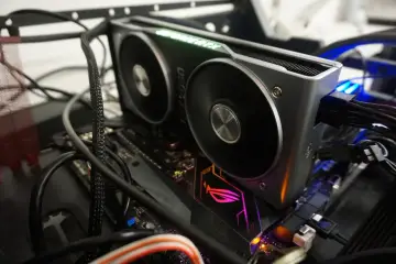 Karta graficzna RTX 2060 z zielonym podświetleniem "GeForce RTX" i dwoma wentylatorami, podłączona do płyty głównej z podświetlanym logo ROG. Dużo kabli, w tym zasilających, otacza komponenty. VRAM tej karty zapewnia płynność w grach.