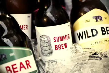 Butelki piwa rzemieślniczego w lodzie. Etykiety "Summer Brew" i "Wild Bear" pomogą Ci zrozumieć, jak czytać etykiety piwa rzemieślniczego, co to jest IBU i BLG.