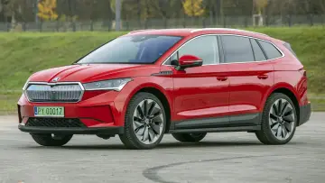 Czerwona Skoda Enyaq na tle zieleni, z tablicą rejestracyjną PY 00017. Ten elektryczny SUV oferuje imponujący zasięg.