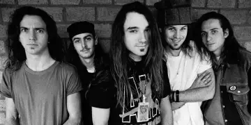 Cinq membres du groupe Pearl Jam posent devant un mur de briques. L'un d'eux porte un t-shirt avec le logo du groupe.