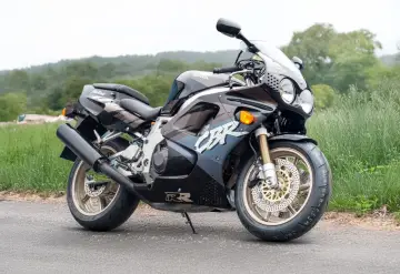 Czarny motocykl Honda CBR 750 Fireblade z lat 90. stoi na drodze, otoczony zielenią.