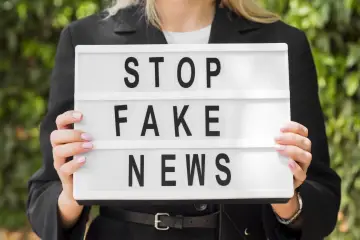 Kobieta trzyma tablicę z napisem "STOP FAKE NEWS", walcząc z dezinformacją.