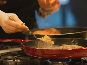 Cebolla caramelizada siendo removida con un tenedor en una sartén roja sobre el fuego.