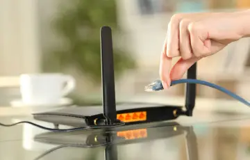 Dłoń podłącza kabel sieciowy do routera TP-Link. Prosty przewodnik, jak ustawić router TP-Link, zaczyna się od tego kroku.