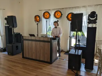 Młody DJ przy konsoli, otoczony sprzętem nagłośnieniowym i oświetleniem. Unikaj błędów w wyborze oprawy muzycznej – DJ czy zespół?