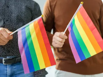 Dwie osoby trzymają tęczowe flagi, symbolizujące różnorodność i akceptację. Dyskusja o przyczynach biseksualizmu jest ważna.
