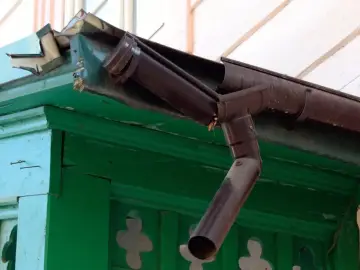 Uszkodzone uszczelnienie rynny plastikowej wymaga naprawy. Brązowa rynna odprowadza wodę z dachu.