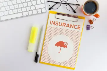 Ubezpieczenie zdrowotne bez pracy: dokument z napisem "INSURANCE" i symbolem parasola. Obok klawiatura, okulary, kawa.