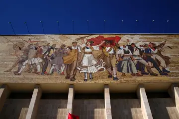 Wielki mural przedstawiający ludzi w strojach ludowych i wojskowych, symbolizujący siłę i jedność. To przykład sztuki socrealizmu, co to za styl?