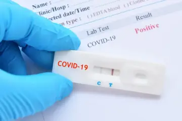 Rękawiczka ochronna trzyma test antygenowy COVID-19 z pozytywnym wynikiem.