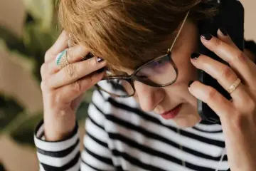 Kobieta w okularach rozmawia przez telefon, martwiąc się, czy pracodawca może rozporządzać urlopem pracownika.