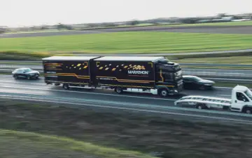 Ciężarówka Marathon International Logistics, z naczepą w barwach firmy, jedzie autostradą. Obok niej mija ją elegancki kabotyn.