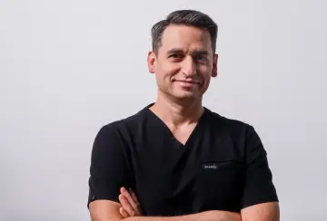 Portret mężczyzny w czarnym scrubie medycznym, ze skrzyżowanymi rękami.