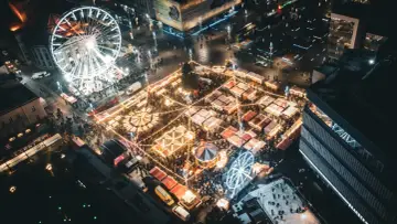 Nocny jarmark bożonarodzeniowy Katowice tętni życiem. Widać karuzelę, diabelski młyn i liczne stoiska rozświetlone tysiącami lampek.