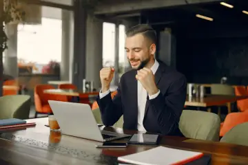 Uśmiechnięty key account manager cieszy się z sukcesu przy laptopie w kawiarni.