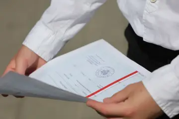 Dłonie trzymają świadectwo z pieczęcią i czerwonym paskiem, symbolizujące szczególne osiągnięcia na świadectwie.