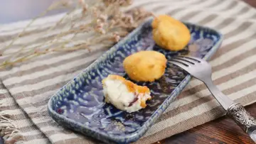 Croquetas de jamón doradas y cremosas en plato azul, una partida.