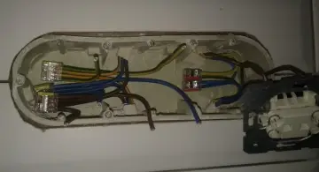 Widok wnętrza puszki instalacyjnej z podłączonymi przewodami elektrycznymi i częścią gniazdka.