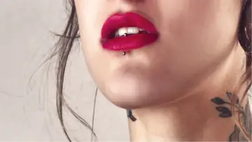 Usta z czerwoną szminką i ashley piercing. Delikatny tatuaż na szyi dodaje uroku.