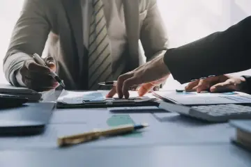 Dwie osoby analizują wykresy i dokumenty. Jedna wskazuje palcem na dane, druga trzyma długopis. Cel: 1000 plus.