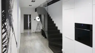 Nowoczesne schody czarne z podstopniami, szklaną balustradą i minimalistycznym wnętrzem.