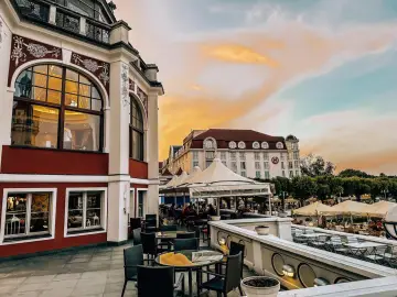 Wieczór w Trójmieście: taras restauracji z widokiem na zabytkową architekturę i zachodzące słońce. Idealne miejsce na romantyczne kolacje i wieczorne spotkania.