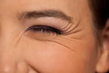 Primer plano de un ojo cerrado con maquillaje, mostrando las arrugas debajo de los ojos que marcan la expresión.