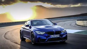 Niebieskie BMW M2 CS pędzi po torze wyścigowym podczas zachodu słońca.