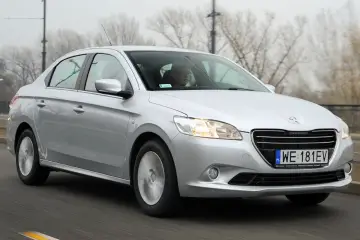 Srebrny Peugeot 301 jedzie po drodze, za kierownicą siedzi mężczyzna w okularach.