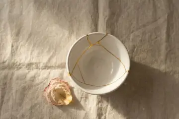Biała miska z pęknięciami zespolonymi złotem, jak w kintsugi, obok zasuszonego płatka róży. Symbolizuje proces leczenia, jak w przypadku osobowości borderline test.