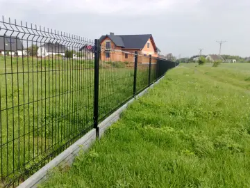 Nowy, czarny płot z podmurówką oddziela posesję z domem od zielonej łąki.