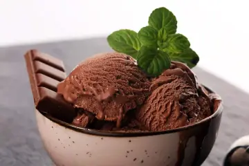 Delicioso helado de chocolate cremoso en un tazón, adornado con una hoja de menta y una barra de chocolate.