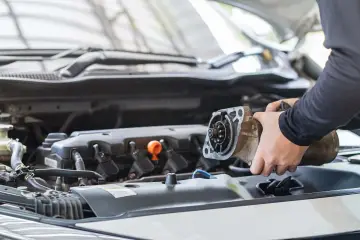 Mechanik wymienia zużyty rozrusznik w samochodzie. Widać jego ręce trzymające element silnika.