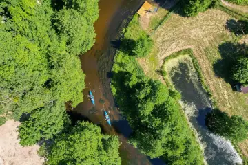 Spływ kajakowy rzeką to jedna z pięknych kociewie atrakcji. Dwie kajaki płyną wśród zielonych drzew.