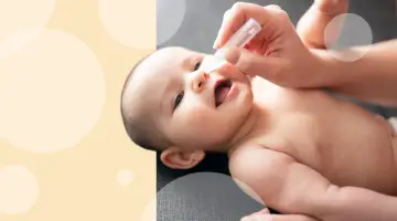 Mama zakrapla kropelki do noska, by ulżyć niemowlakowi z zatkanym nosem. Dziecko patrzy z zaciekawieniem.