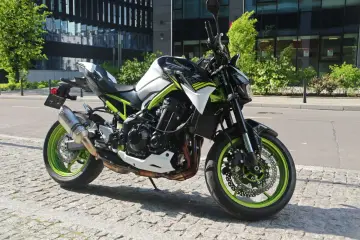 Kawasaki Z900 w miejskiej scenerii, z zielonymi felgami i sportowym wydechem Akrapovič.