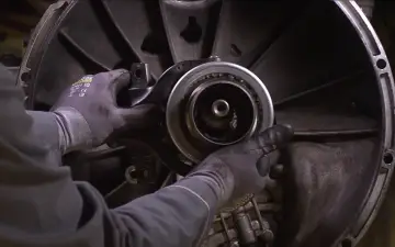 Mechanik w rękawicach wymienia łożysko oporowe w skrzyni biegów.