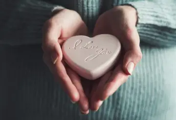 Dłonie trzymają różowe serce z napisem "I Love You". To symbol miłości agape, bezwarunkowej i czystej.