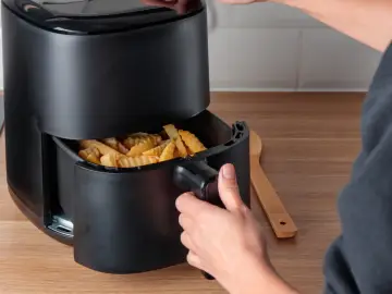 Ręka wyjmuje koszyk z frytkami z frytkownicy beztłuszczowej. To pokazuje, jak działa air fryer co to jest.