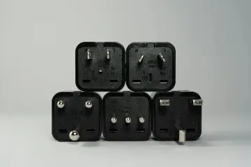 Pięć czarnych wtyczek elektrycznych, każda z oznaczeniem 250V, pokazuje różne normy napięcia w sieci.