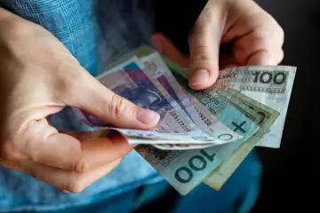 Dłonie trzymające polskie banknoty. Czy to wystarczy na pokrycie minimalnej stawki godzinowej?