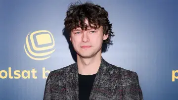 Mateusz Kościukiewicz, znany z wielu świetnych mateusz kościukiewicz filmów, na tle niebieskiej ścianki z logo.