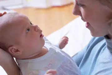 Uśmiechnięta mama patrzy na swoje 6 tygodniowe dziecko, które z zaciekawieniem spogląda w górę.
