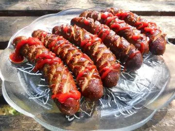 Kiełbasa z grilla inaczej: nacięta i polana ketchupem, ułożona na szklanej paterze. Idealna na letnie popołudnie.