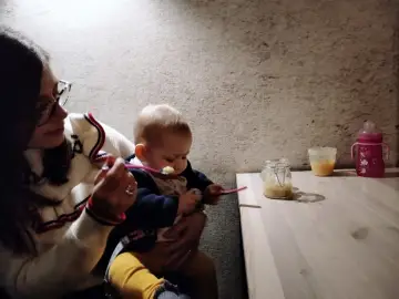 Mamma dà la pappa al suo bimbo fuori casa, con un vasetto di omogeneizzato e un biberon pronti.