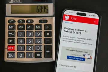 Kalkulator i smartfon z aplikacją KSeF. Na ekranie telefonu widoczna jest informacja o Krajowym Systemie e-Faktur, który ułatwia wystawianie i odbiór faktur, także tych bez VAT.